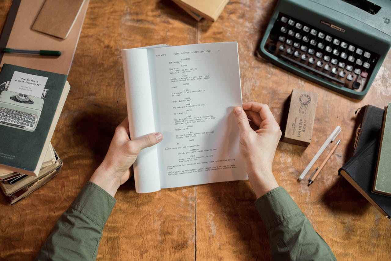Hands holding script page at vintage desk with typewriter and books.